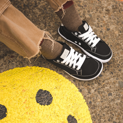 Close up picture of the FREESTYLE 3 Coal being worn by a woman sitting on a pavement surface, a yellow smiley face shown painted on the pavement. 